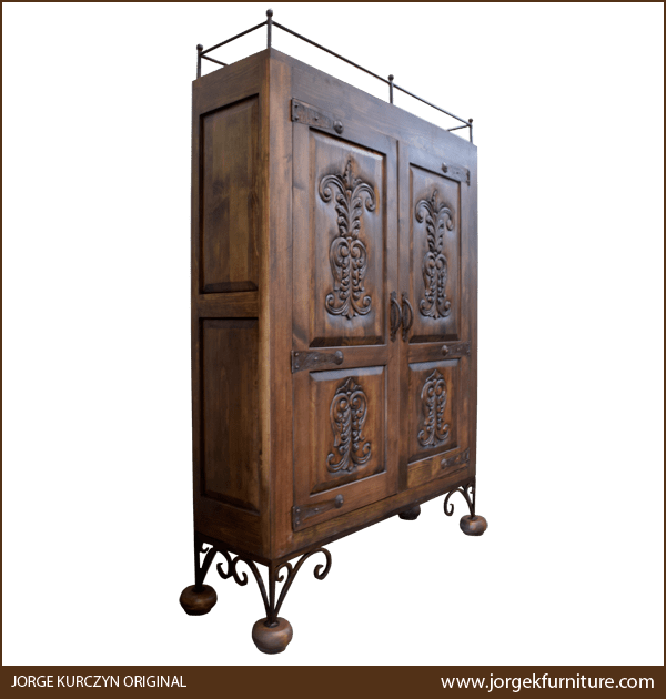 Three-quarter angle of artisan-crafted armoire showing carved panels and forged iron supports